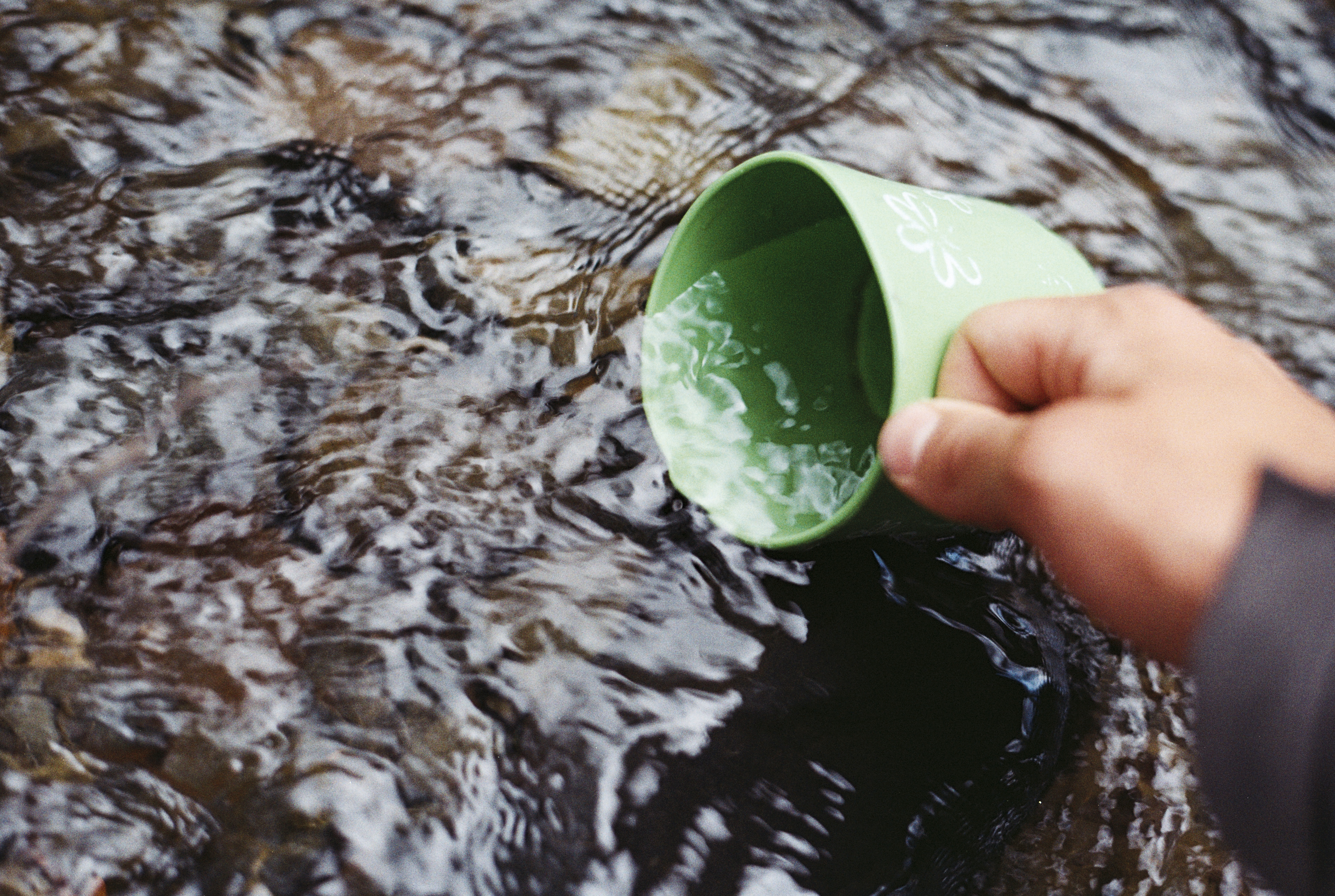 Photo of hand filling cup of water in river by Jens Johnson